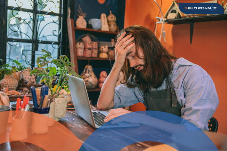 Artigiano seduto al banco di lavoro con il computer portatile, visibilmente pensieroso, in un laboratorio creativo. L’immagine rappresenta la difficoltà di farsi trovare online dopo aver creato un sito web.